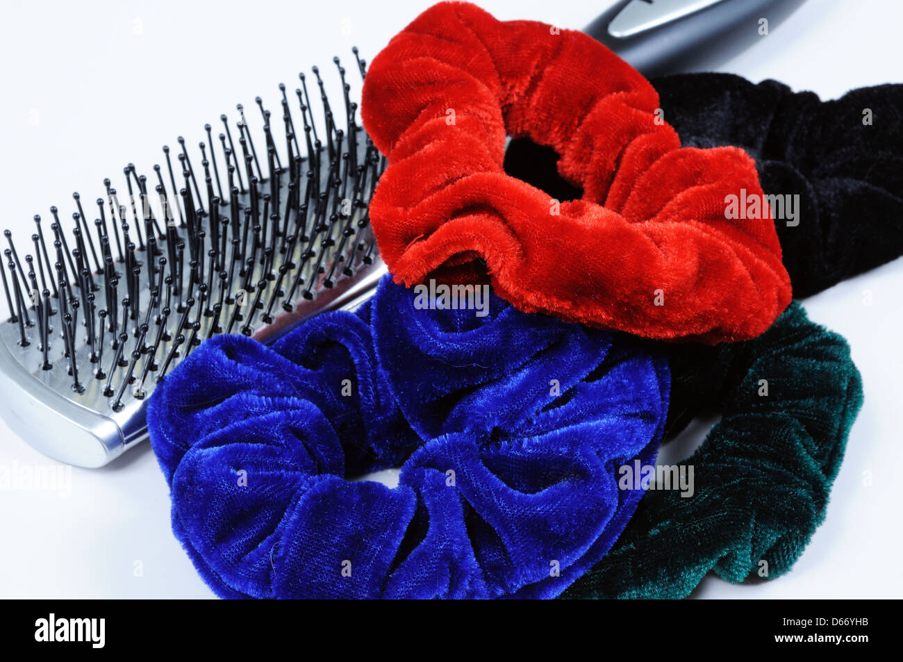 Four velvet hair scrunchies and a hairbrush against a white background. Stock Photo
