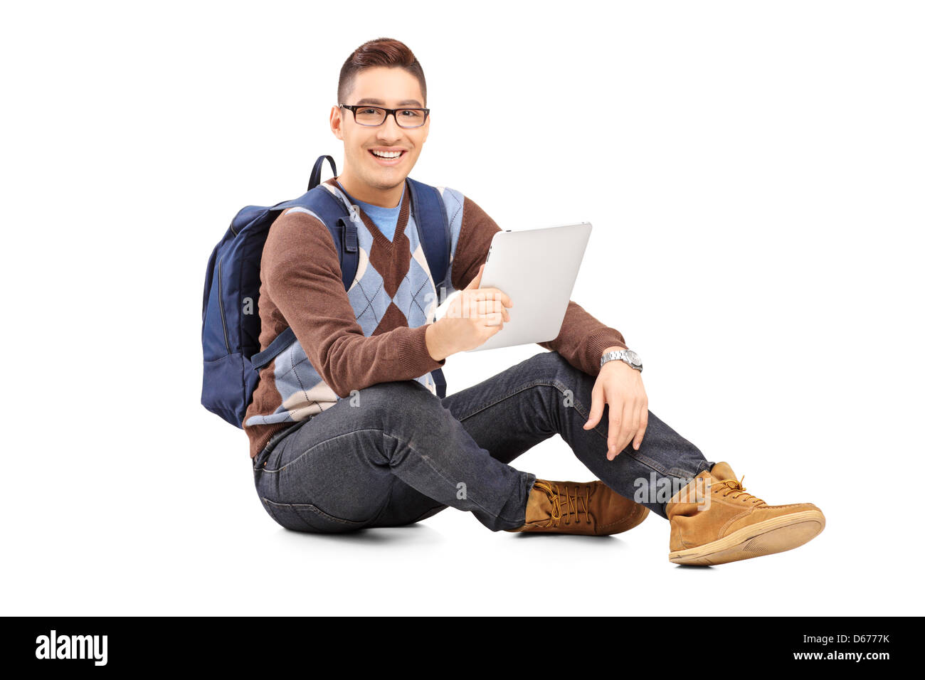 Smiling male student with backpack seated on a floor holding a tablet ...