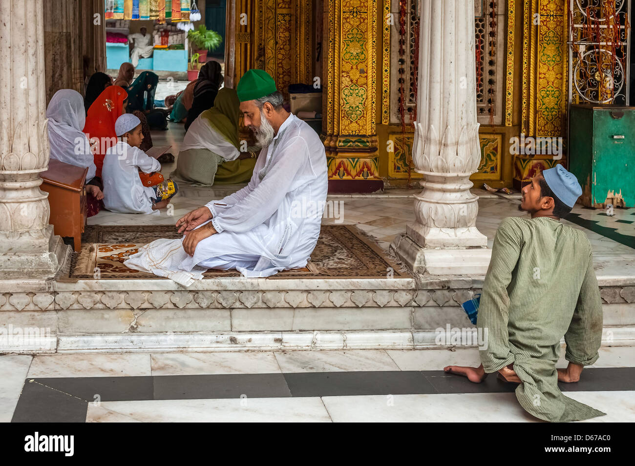 A man with green hat prays whilst disabled beggar waits patiently for alms at mosque in Nizamuddin, Old Delhi, Delhi, India. Stock Photo