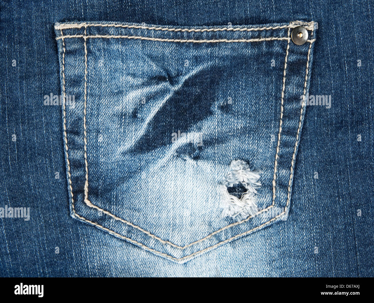 Hole in a pocket of worn out old blue jeans. Stock Photo