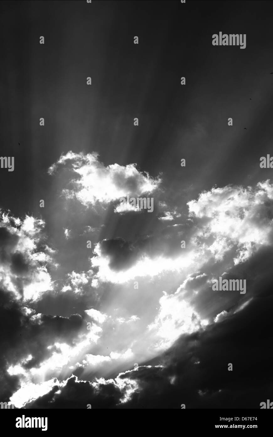 A black and white photograph capturing dramatic sun rays breaking through the clouds. The image showcases dynamic lighting and natural contrasts in the sky, with a focus on sun traces. Stock Photo