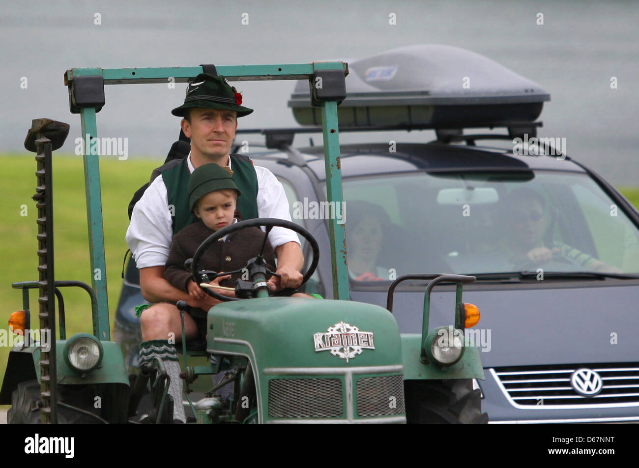 In traditional Bavarian garb, a man drives a tractor with his son during an oldtimer tractor meeting in Buching, Germany, 17 June 2012. Photo: Karl-Josef Hildenbrand Stock Photo