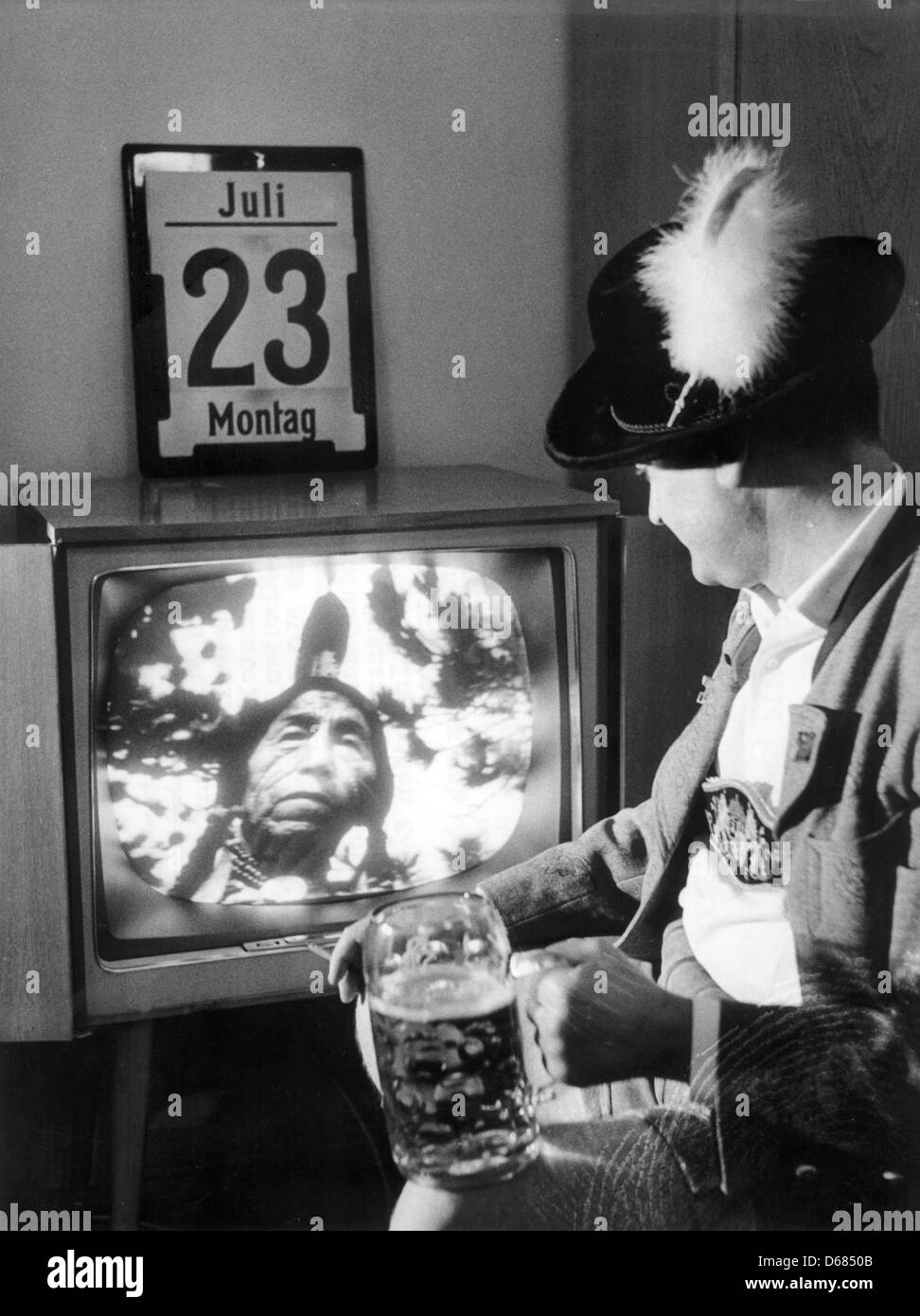 (dpa FILE) - An archive picture, dated 23 July 2012, shows a Bavarian man in traditional clothing cheering with a glass of beer while watching the live broadcast of a western on his television set at his home in Bavaria, Germany, 23 July 1962. The civilian communications satellite Telstar was launched from Cape Canaveral on 10 July 1962 enabling the first live broadcast of televise Stock Photo