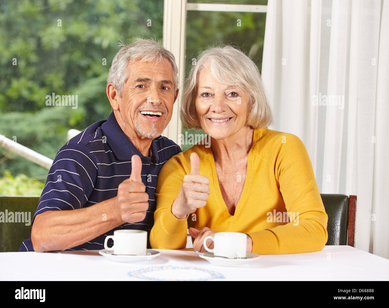 Happy senior couple holding thumbs up at coffee table Stock Photo - Alamy