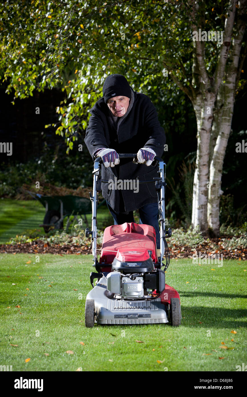 Old man doing the gardening, mowing the lawn. Stock Photo