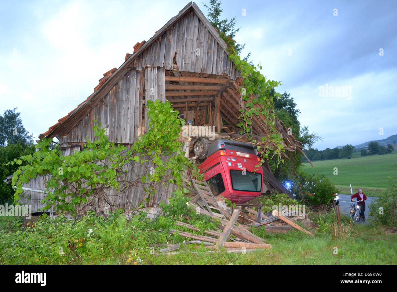 Fire fighters stand in front of a barn into which a red mimi van has  crashed near Kulmbach, Germany, 18 July 2012. An 18 year old driver was  involved in an accident