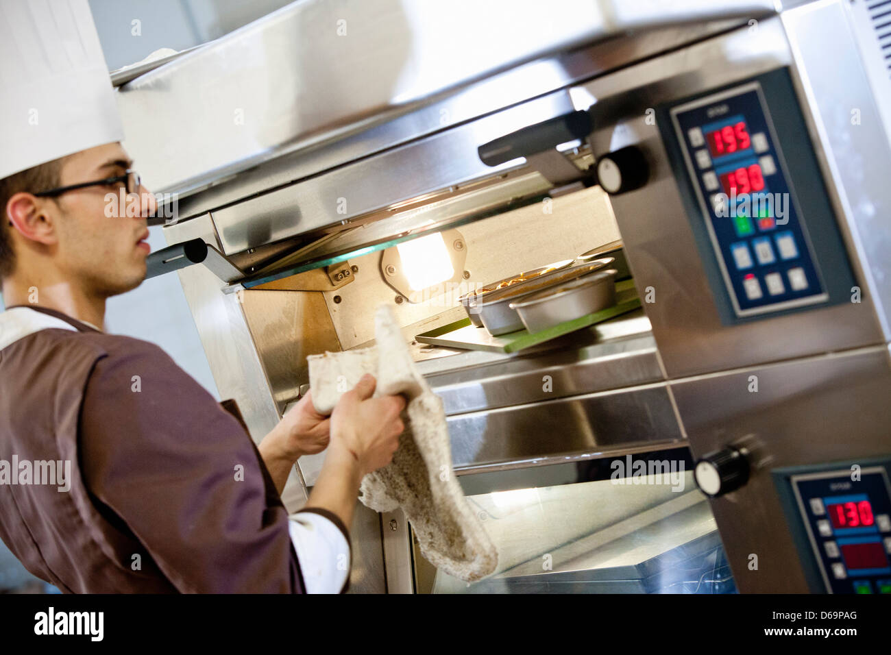 Baker putting food in oven in kitchen Stock Photo Alamy