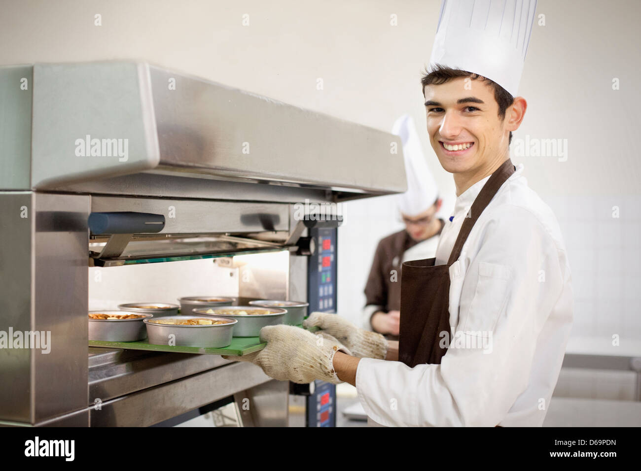 Baker putting food in oven in kitchen Stock Photo Alamy