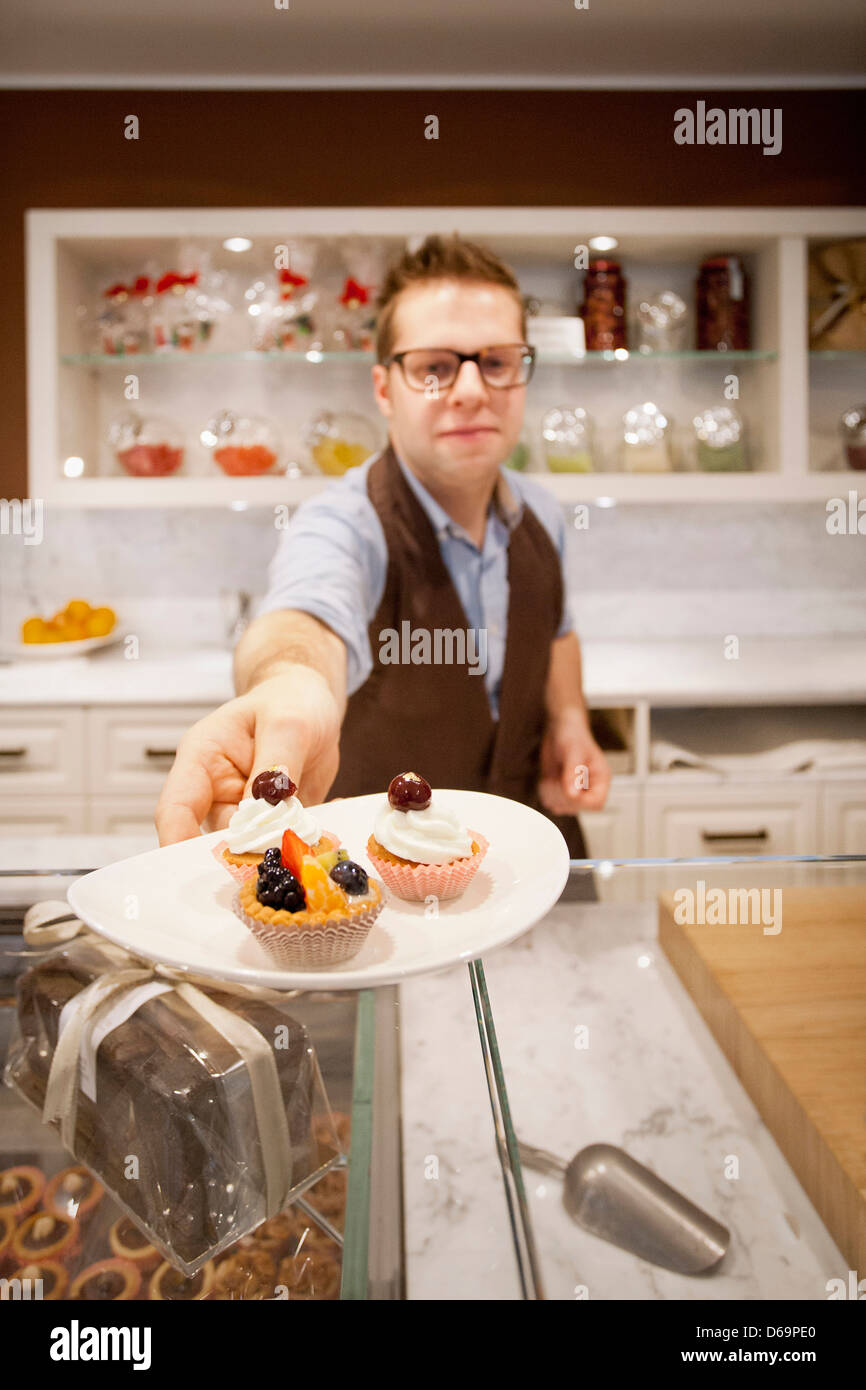 Cashier holding plate of tarts in bakery Stock Photo