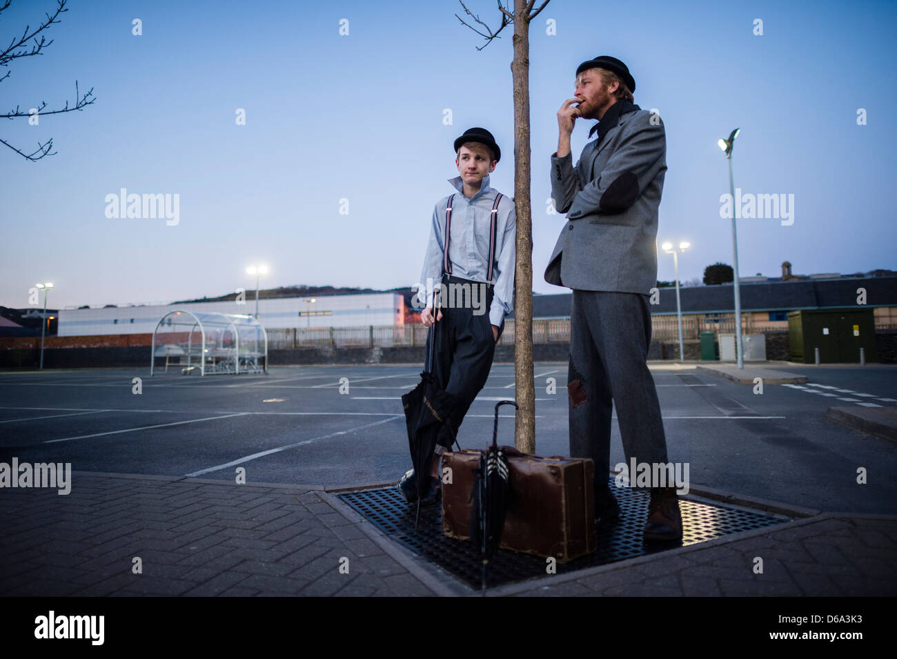 2 male actors performing as Vladimir & Estragon in Samuel Beckett's classic play 'Waiting for Godot' in a deserted car park outdoors  at night, UK Stock Photo