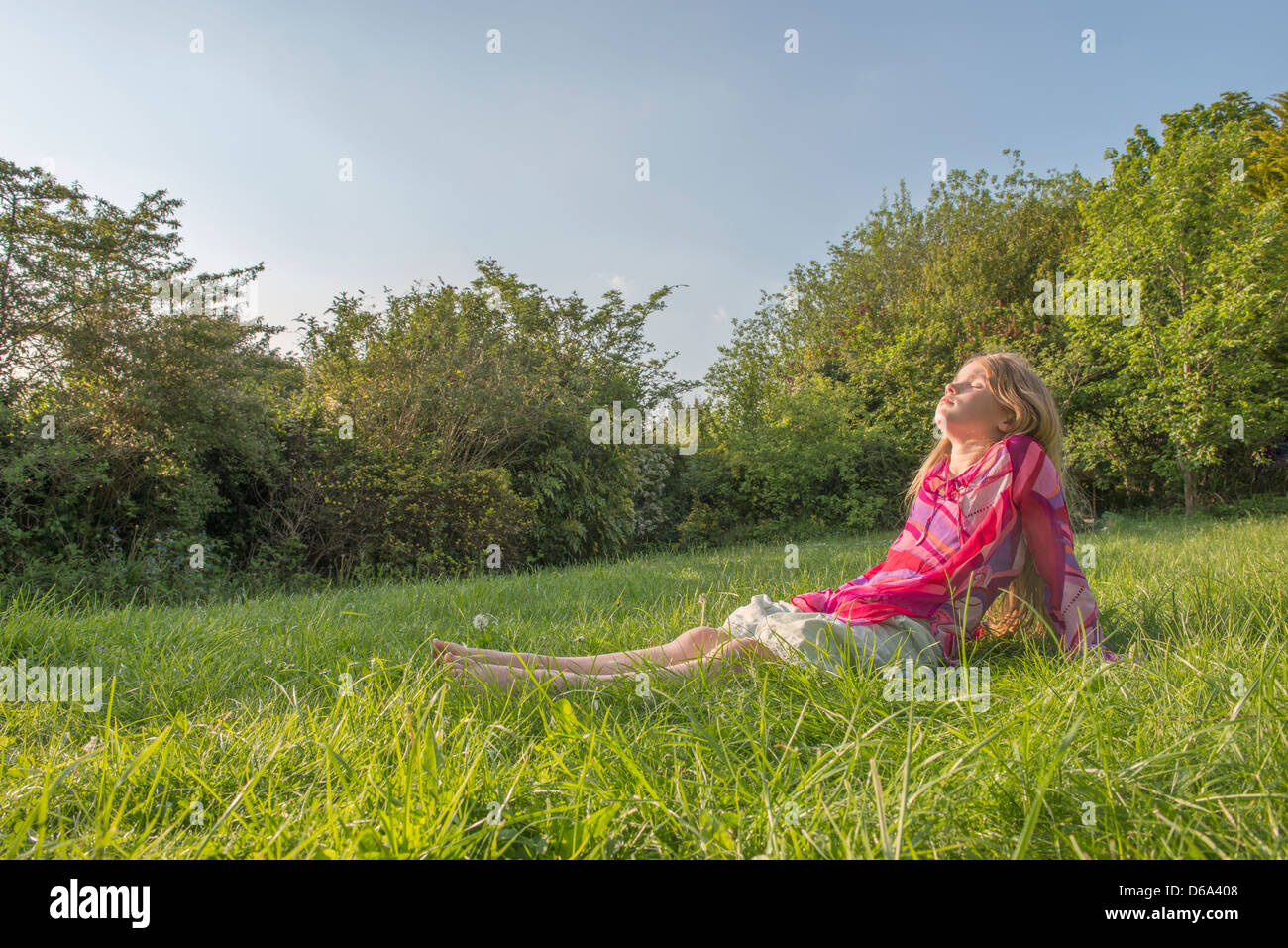 Girl sitting in grassy field Stock Photo