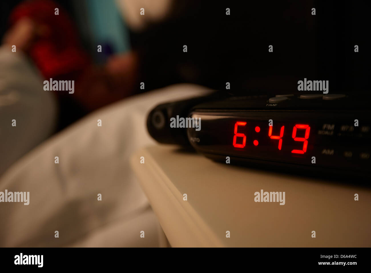 alarm clock early morning with early twenties woman lying turning in bed in a bedroom Stock Photo