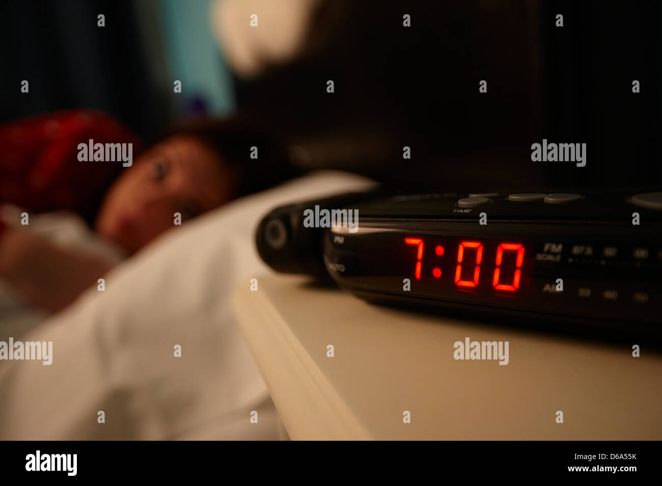 alarm clock early morning with early twenties woman lying in bed in a bedroom Stock Photo