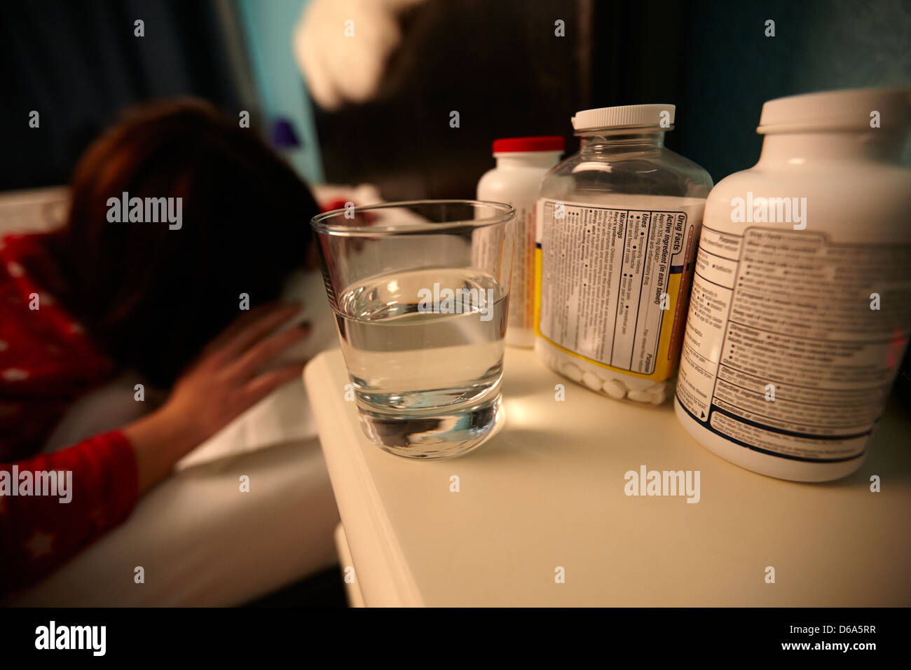 glass of water and bottles of pills on bedside table of early twenties woman waking in bed in a bedroom Stock Photo