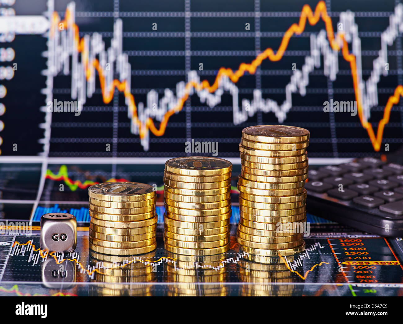 Uptrend stacks coins, dices cube with the word GO and calculator on the financial stock charts as background. Selective focus Stock Photo
