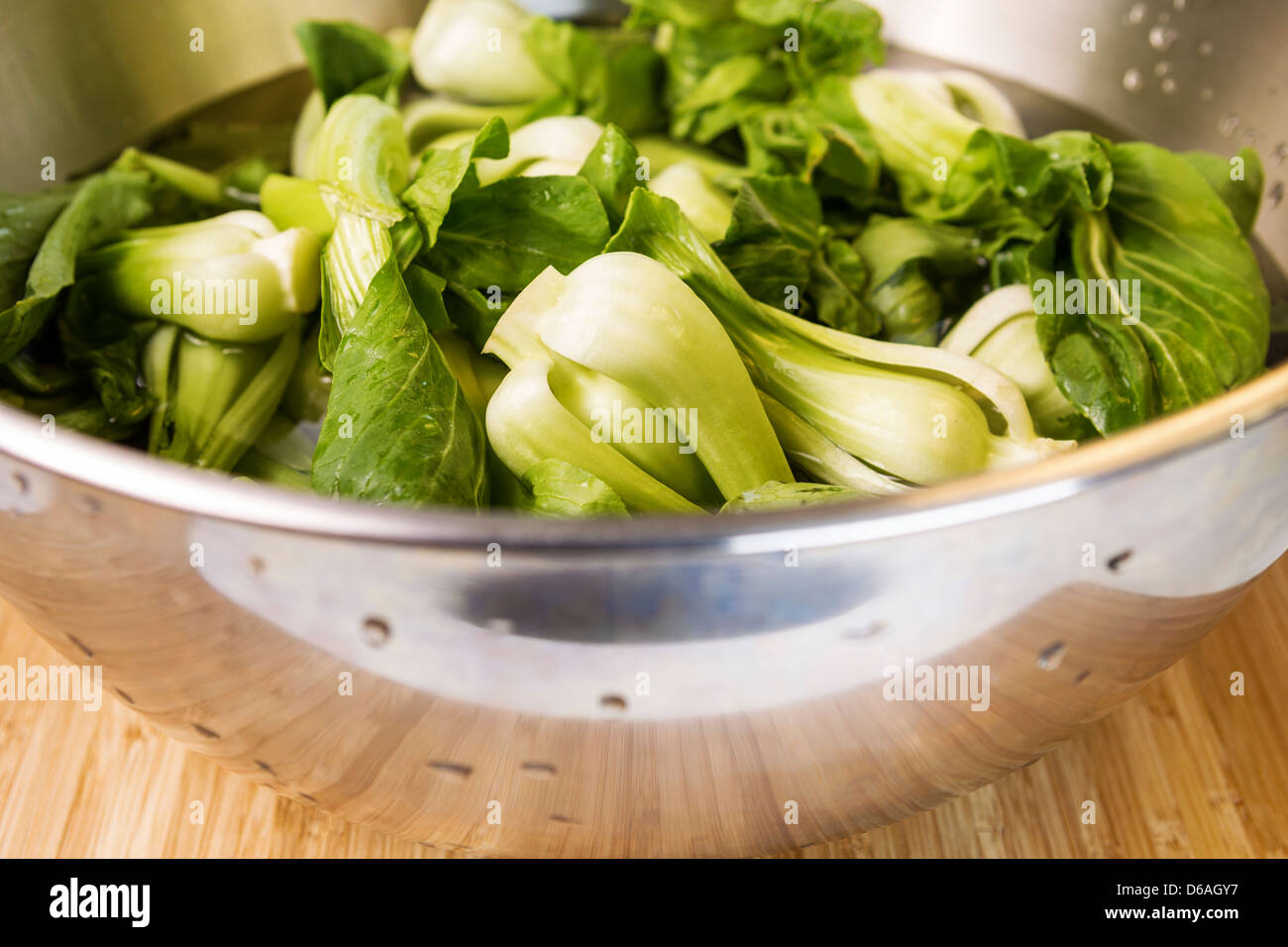 Closeup horizontal photo of washed Chinese Choy in Stainless Steel bowl on natural bamboo wood Stock Photo