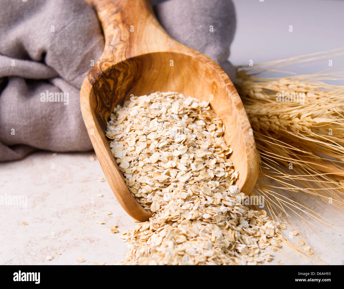 Horizontal photo of rolled oats in wooden spoon with cloth napkin and wheat stalks on natural white stone Stock Photo