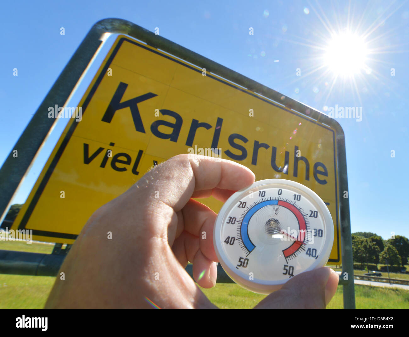 A thermometer is hold in front of the placename sign in Karlsruhe