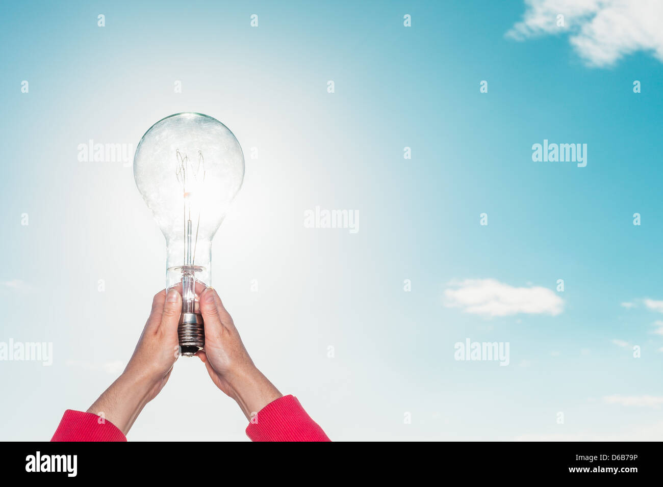 Woman holding light bulb in sky Stock Photo