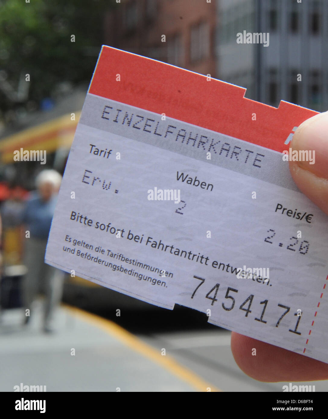 ILLUSTRATION - An illustrated picture shows a single ticket held in front of a street car in downtown Karlsruhe, Germany, 28 August 2012. Ticket prices for busses and streetcars will increase again in south-west Germany. Rising gas prices and sinking numbers of pupils are responsible for the price increases. Photo: Uli Deck Stock Photo