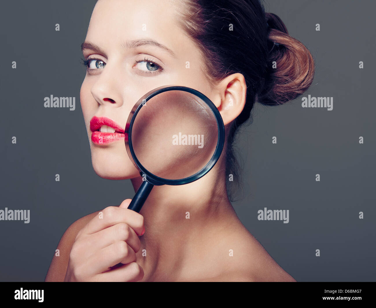 Woman holding magnifying glass to face Stock Photo