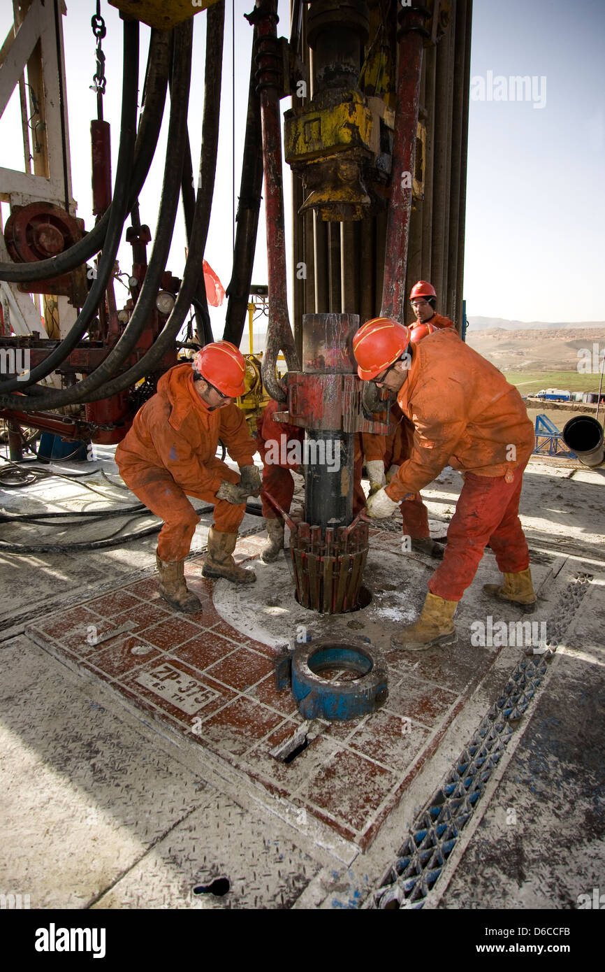 Onshore oil and gas exploration rig with crewmen handling wellhead safety clam to hold casing before drilling Kurdistan Iraq Stock Photo