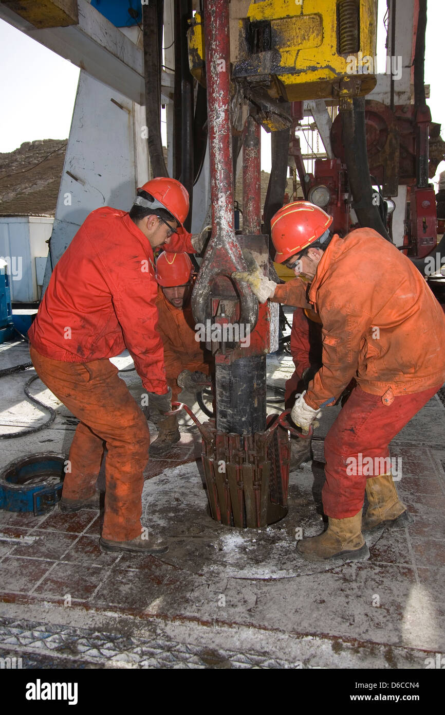 Onshore oil and gas exploration rig with crewmen handling wellhead safety clam to hold casing before drilling Kurdistan Iraq Stock Photo