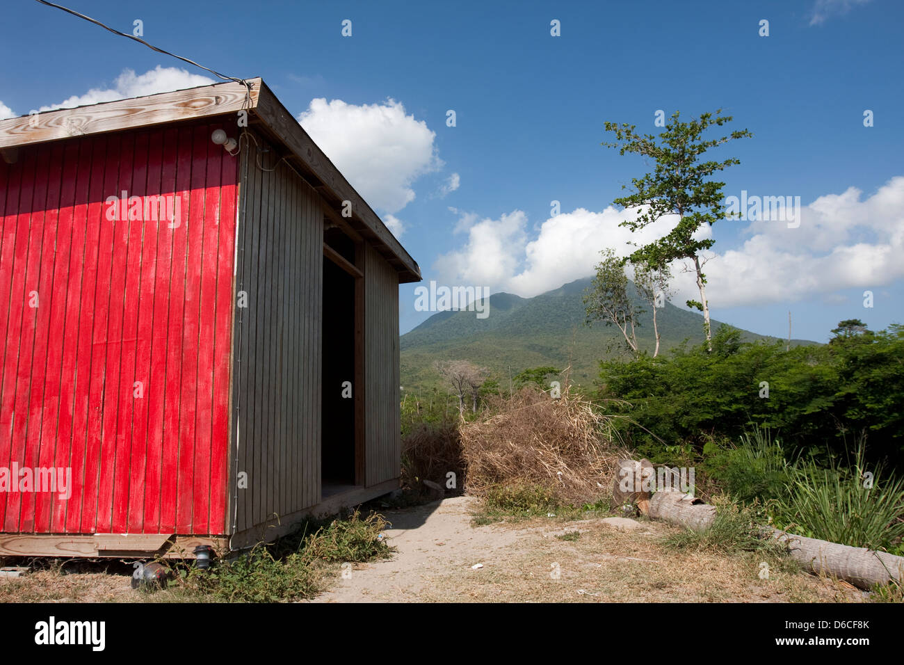 Nevis Peak in the distance beyond a red painted wood shed on the Caribbean island Stock Photo