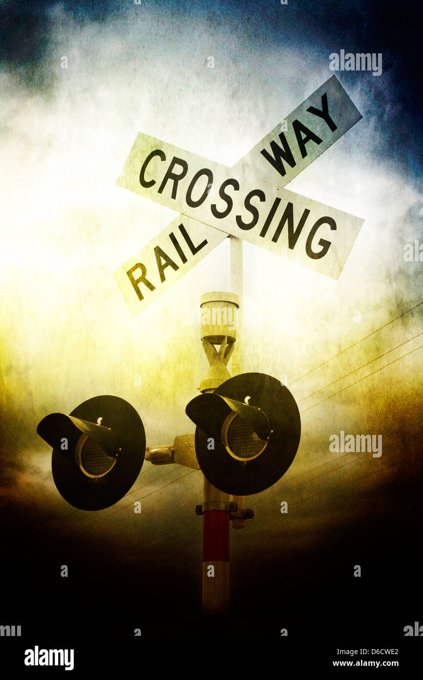 A low angle atmospheric view of a railway crossing sign and stop lights under a moody sky. Stock Photo