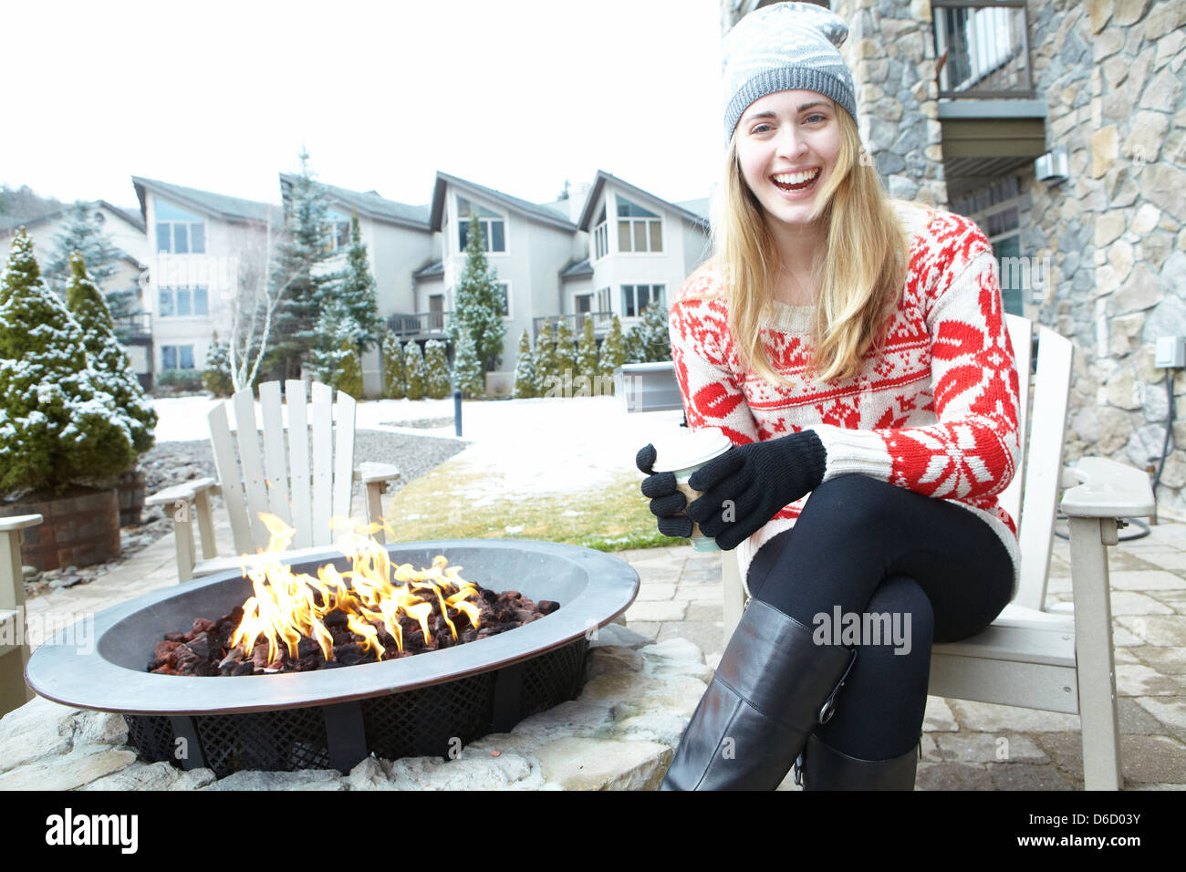 Girl with coffee in hand sitting in front of outdoor fireplace Stock Photo