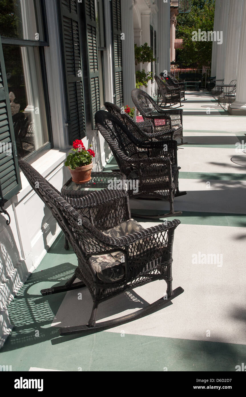 Photograph of black wicker rocking chairs on large, spacious Southern veranda with pots of Geraniums on small tables. Stock Photo