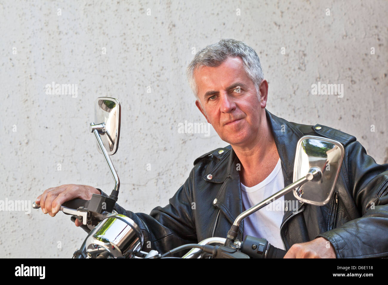 Capture of a Caucasian motorbiker in casual attire and relaxed expression looking into lens sat on a red cruiser. Stock Photo