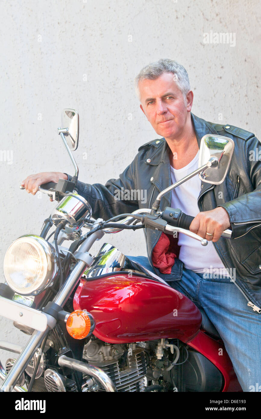 Portrait of a Caucasian motorbiker in casual attire tight lipped looking into lens sat on a red cruiser. Generic shot location Stock Photo