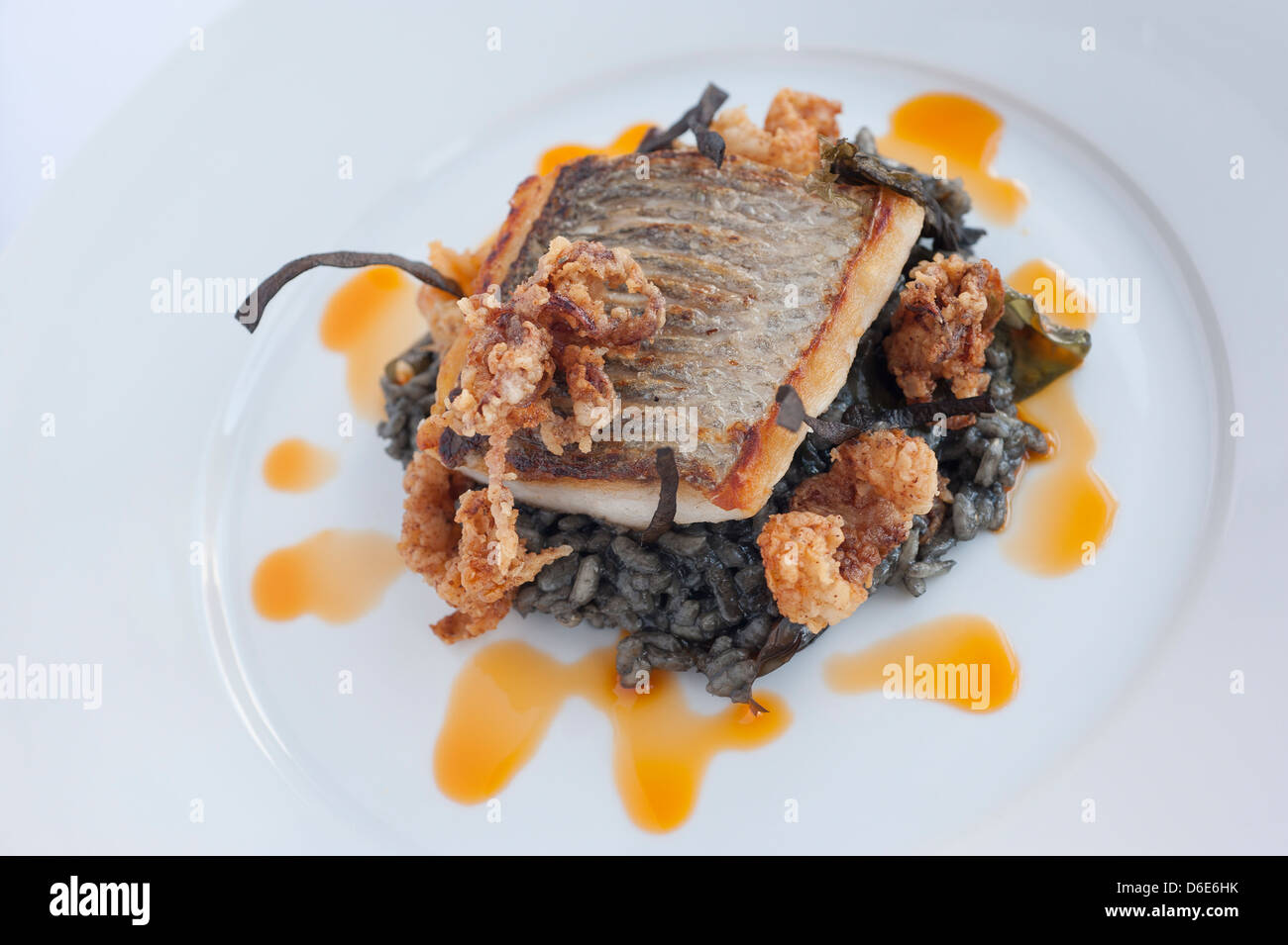 Wild bass, squid ink risotto, calamari, mermaids grass and chorizo oil Stock Photo