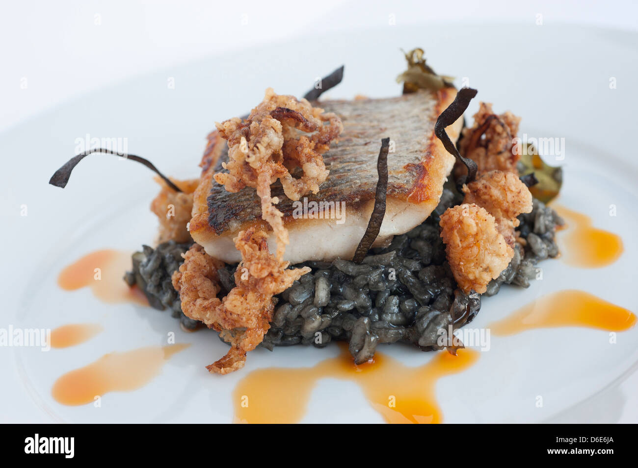 Wild bass, squid ink risotto, calamari, mermaids grass and chorizo oil Stock Photo