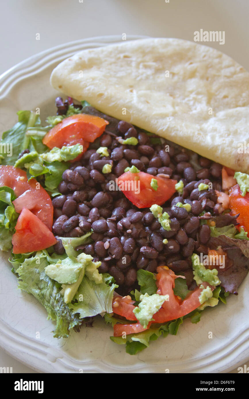 Close up of a plate filled with black beans, avocado, tomato, lettuce, greens and a white flour tortilla Stock Photo