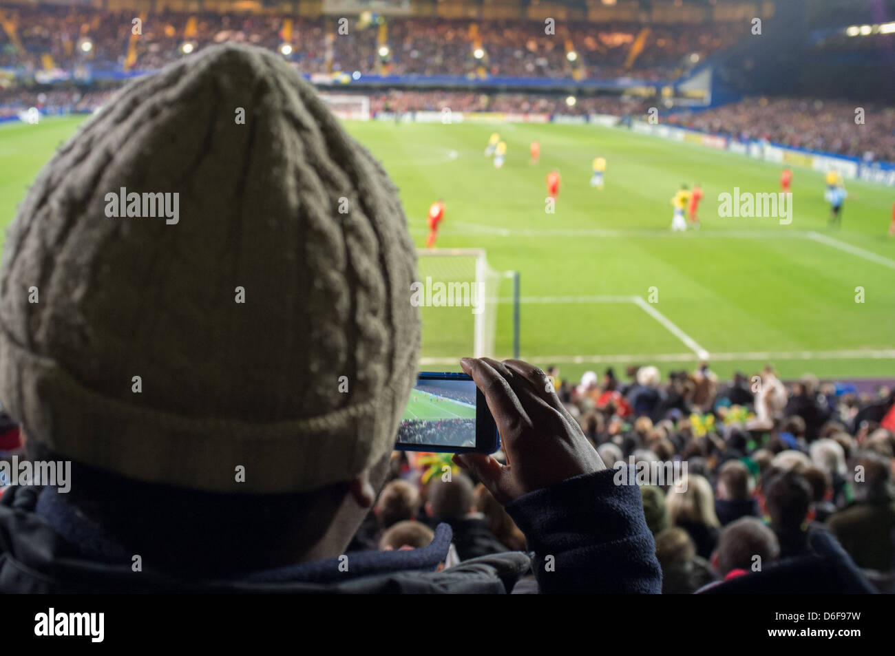 A male spectator takes a picture of a football match on his mobile phone. Stock Photo