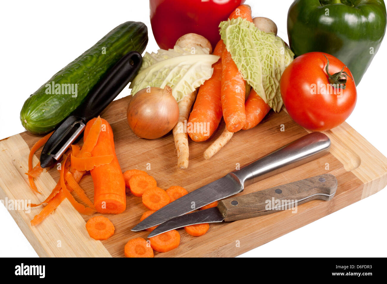 Vegetables, knife and peeler on cutting board isolated on white