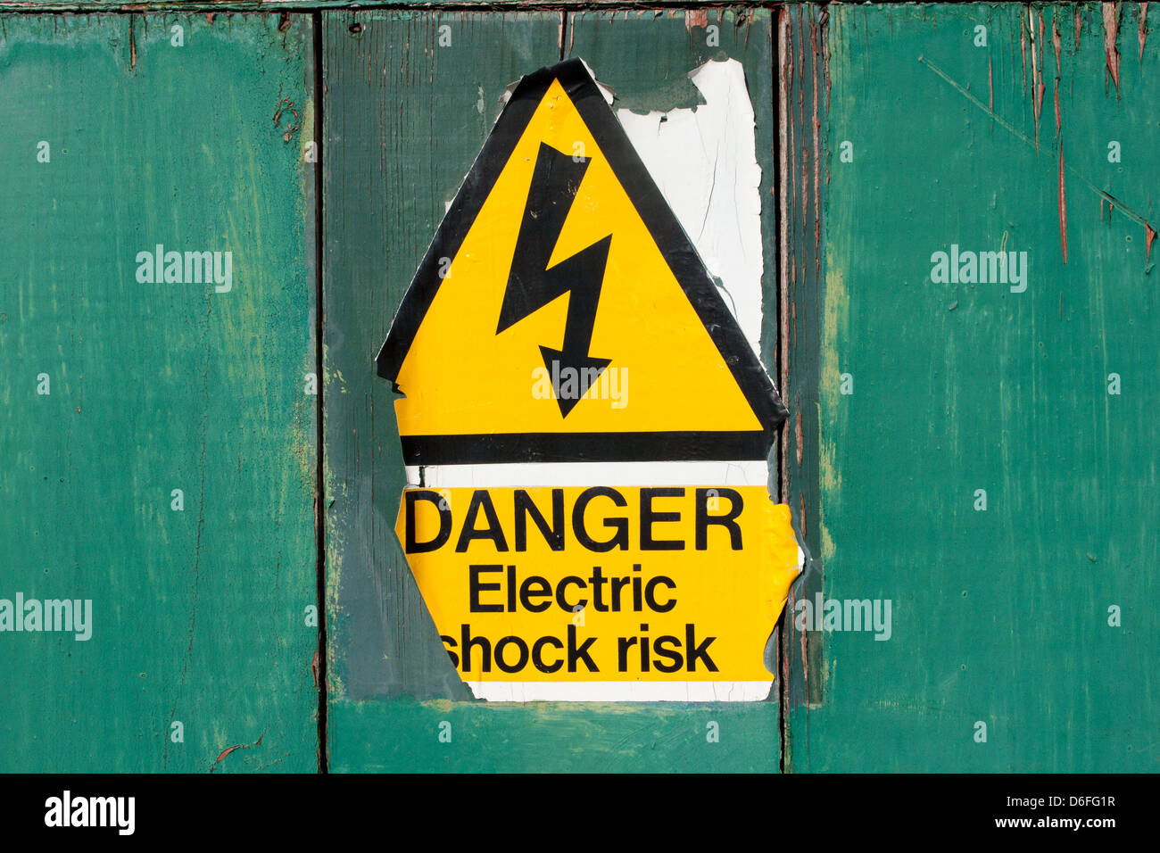 An old  and peeling 'Danger Electric shock risk' sign on a painted green background in Bristol, U.K.. Stock Photo