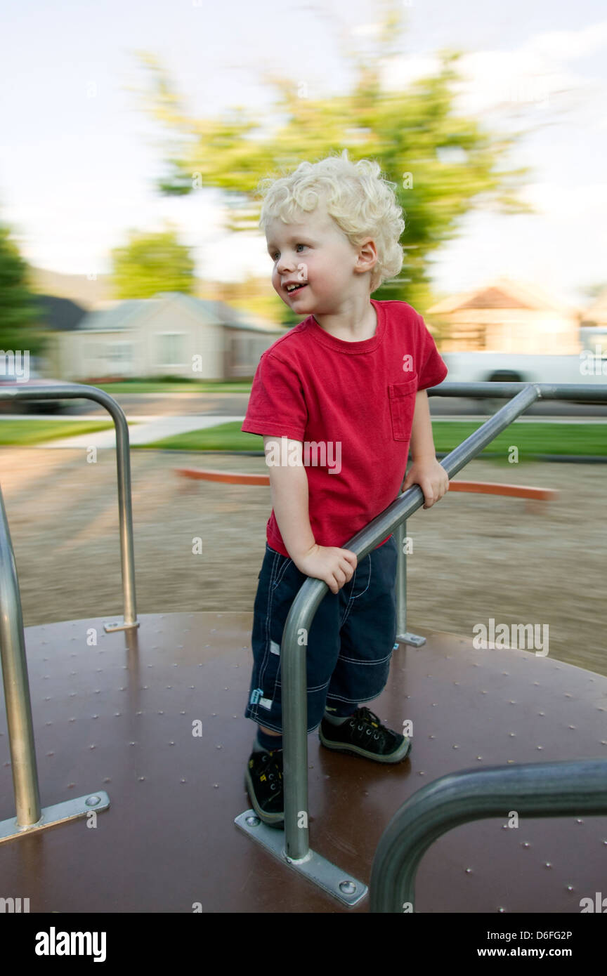 Blonde haired boy playing on a merry-go-round in a park on the playground. Stock Photo