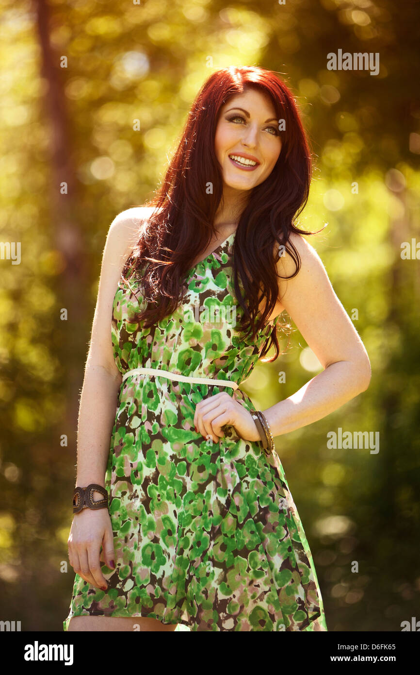 Woman in green flower dress standing outside in front of trees Stock Photo