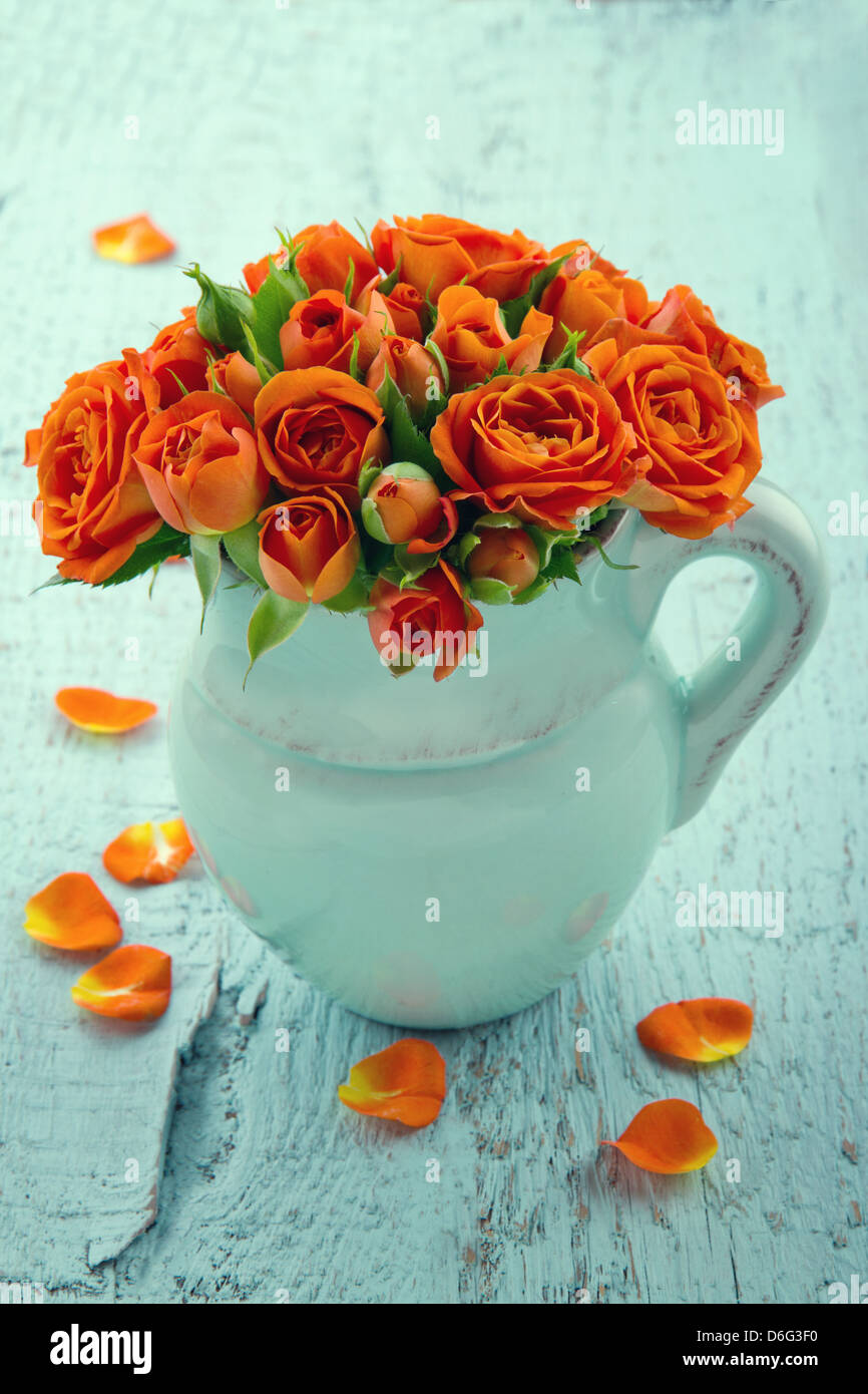 Bouquet of orange roses in a blue vase on vintage wooden shabby chic background Stock Photo