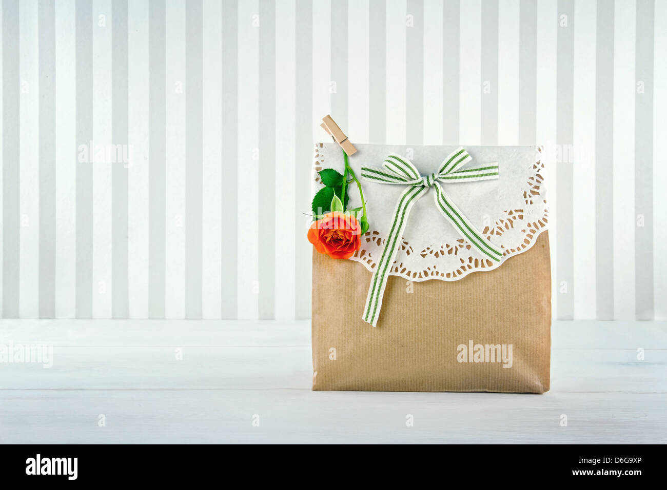 Brown paper gift bag decorated with doily, orange rose and green striped ribbon Stock Photo