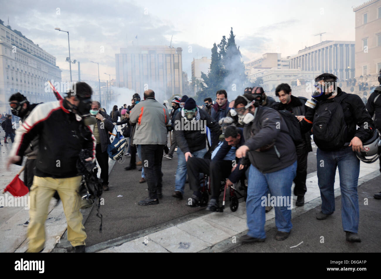 Musician Mikis Mikis Theodorakis (C-86), who is wearing a gas mask in the picture, collapses during a demonstration and is seated in a wheelchair by companions in Athens, Greece, 12 February 2012. Mikis Theodorakishas had to cancel his attendance at a demonstration against an austerity programme of the Greek government, due to breathing troubles. Photo: Wassilis Aswestopoulos Stock Photo
