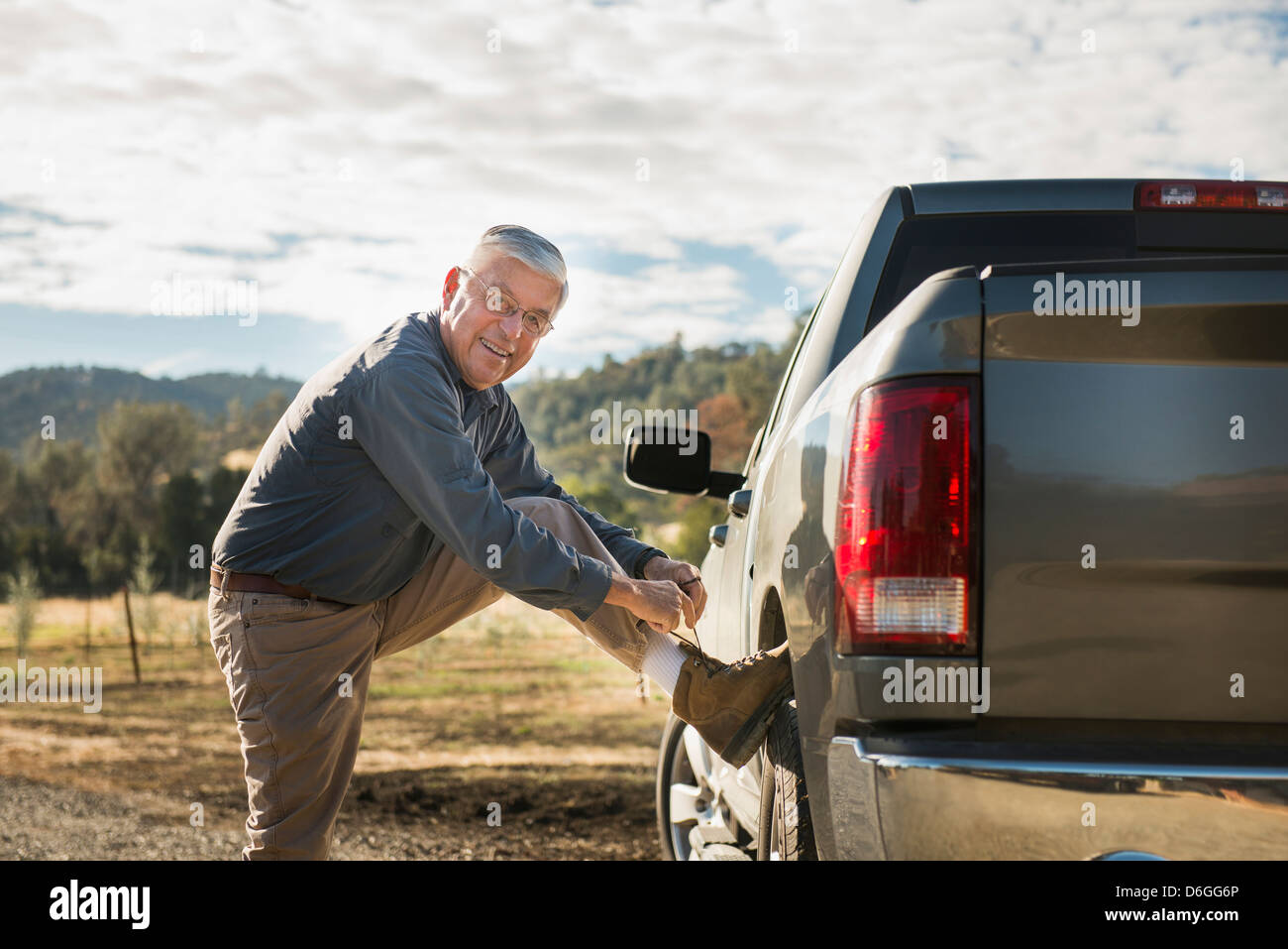 Older Caucasian man tying his shoe on truck wheel Stock Photo