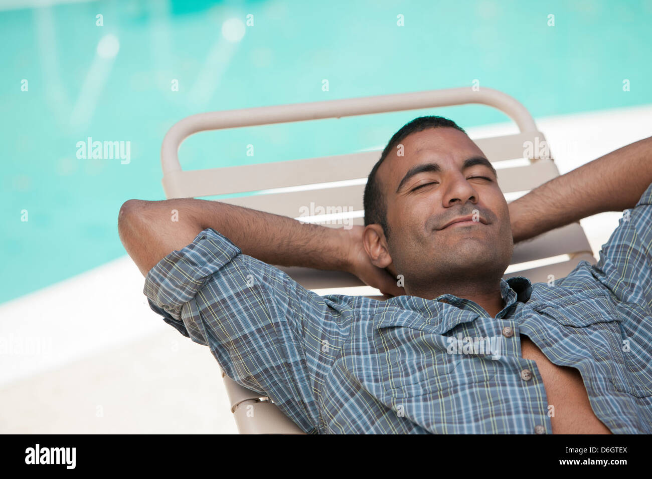 Man relaxing in lawn chair by pool Stock Photo