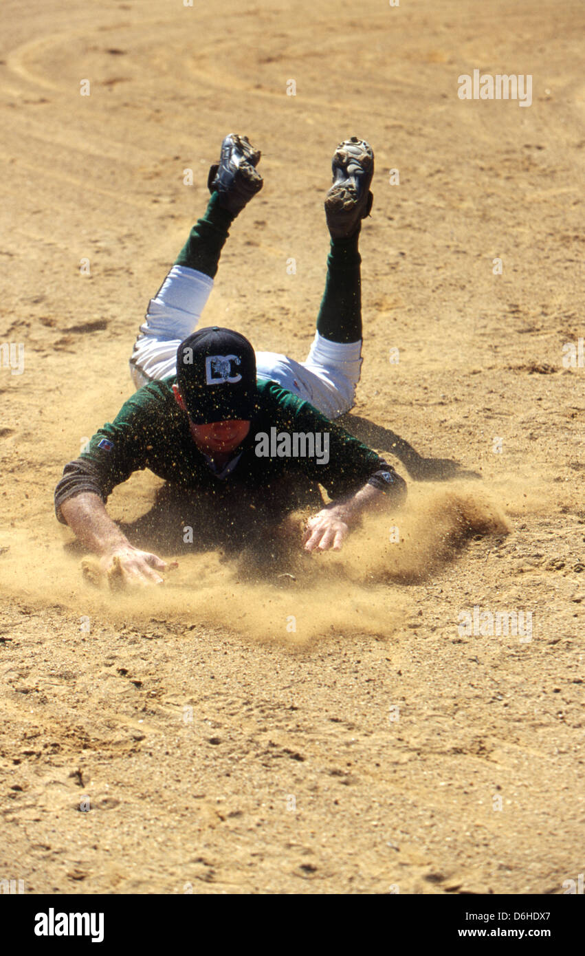 High school baseball player slides in a cloud of dirt into third base. Stock Photo