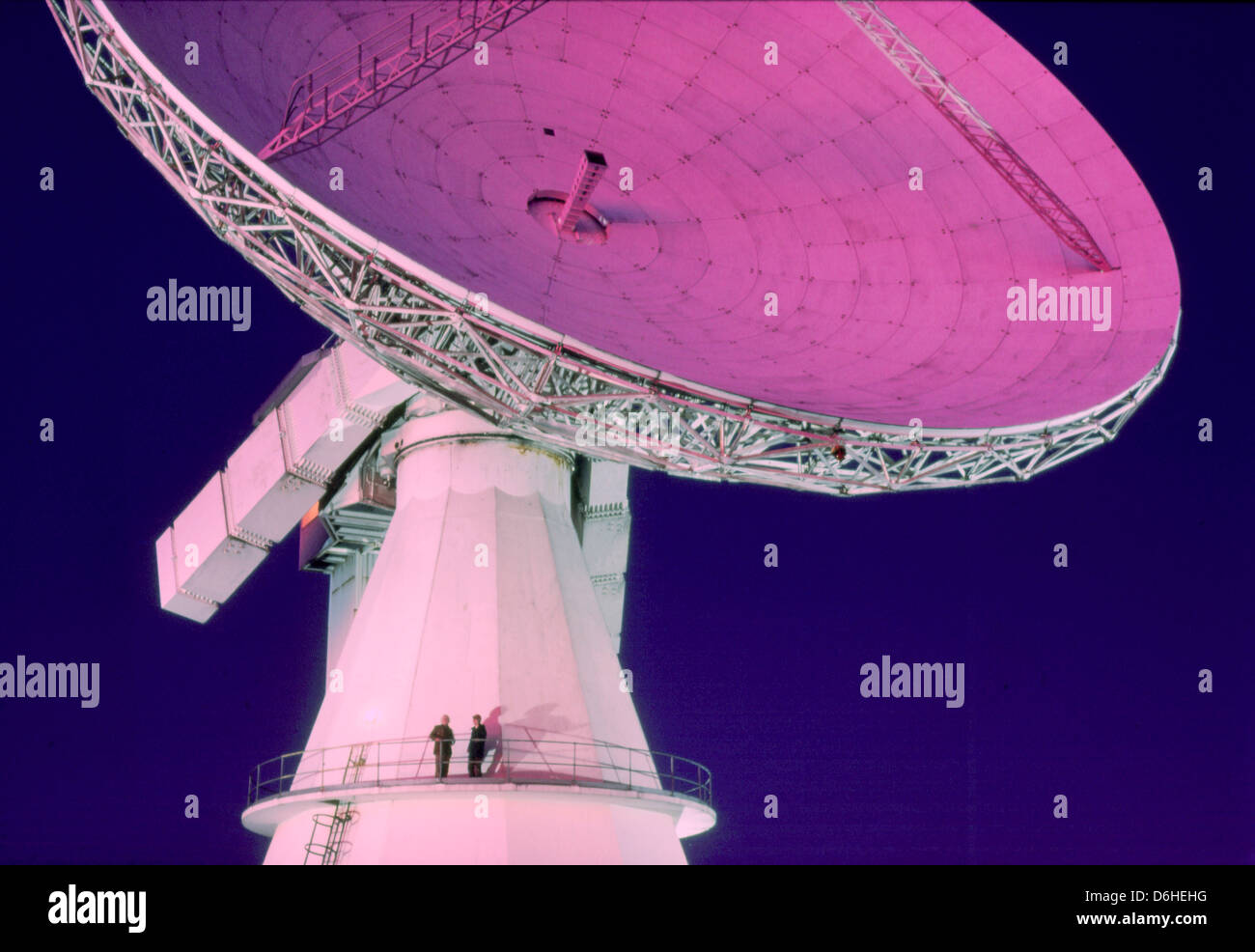 Night view of technicians standing on platform of telecommunications (satellite) dish, Cornwall, England Stock Photo