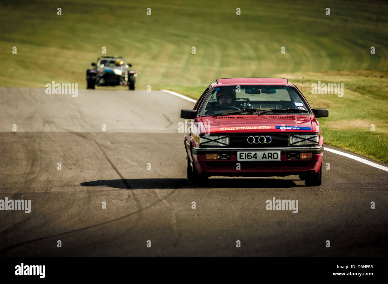 Audi car racing at Cadwell park race track being followed by a Caterham sports car on a sunny day. Stock Photo