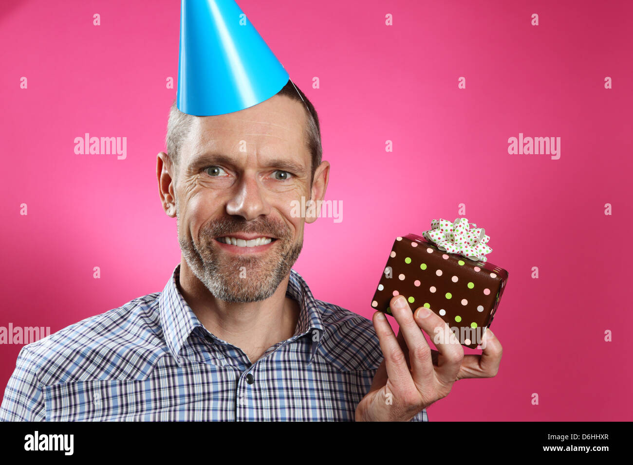 Man wearing a party hat with a toothy smile and holding a gift. Stock Photo